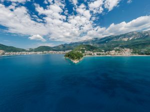 A stunning aerial view of a coastal town framed by mountains and blue ocean under a cloudy sky.